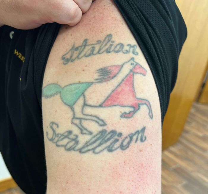 Tattoo of a misspelled phrase Italian Stallion with a poorly drawn horse in red and green ink on upper arm.