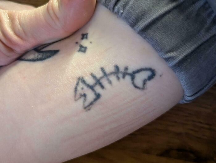 Close-up of a poorly done fish bone tattoo on a person's arm, showcasing bad tattoos that lack careful thought.