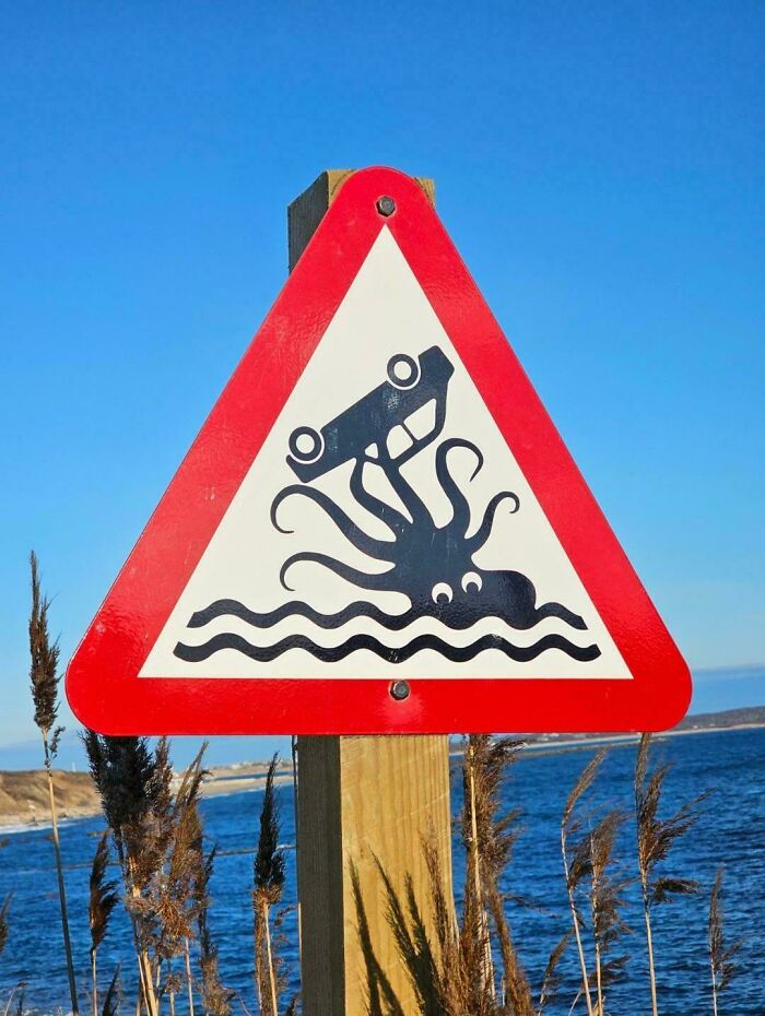 Funny and bizarre warning sign showing an octopus lifting a car near the water by the coast.