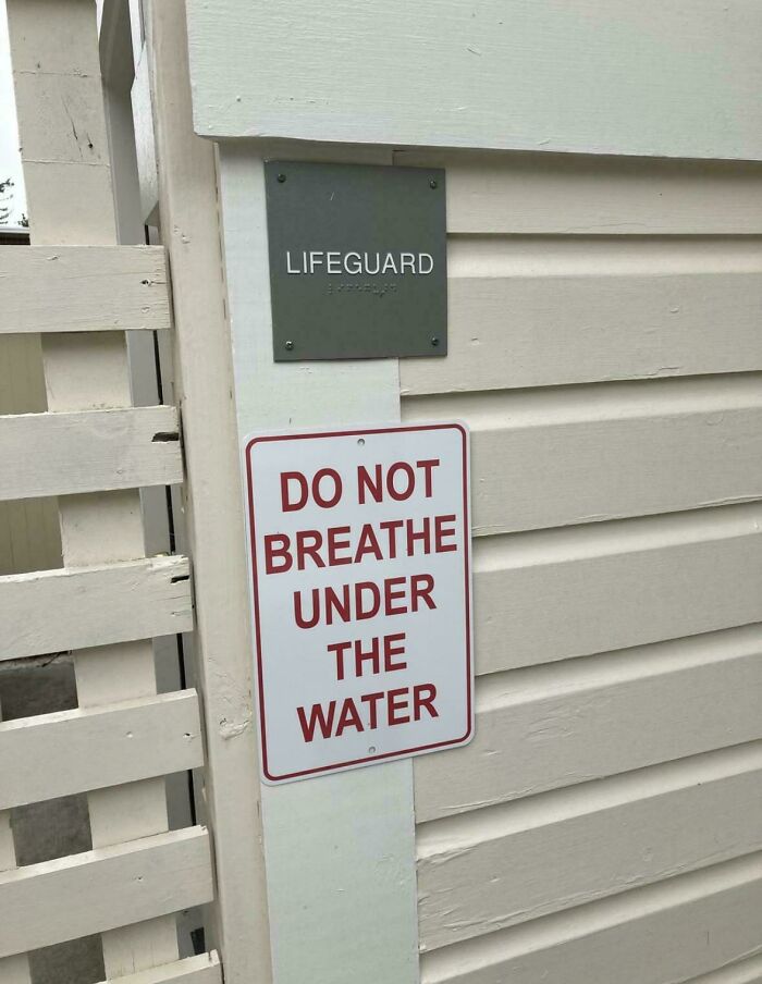 Absurd and hilarious sign reading do not breathe under the water posted near a lifeguard station on a beige wall.