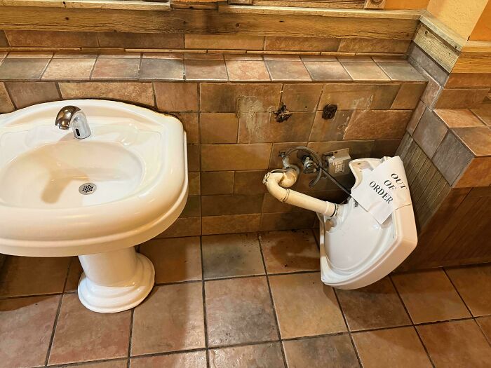Broken sink with an out of order sign in a tiled bathroom, showcasing a bizarre and hilarious sign you don’t see every day.