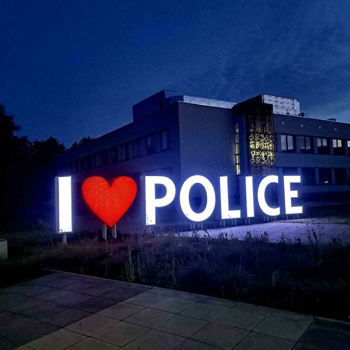 Illuminated sign at night displaying I heart police outside a modern building in a quiet setting.