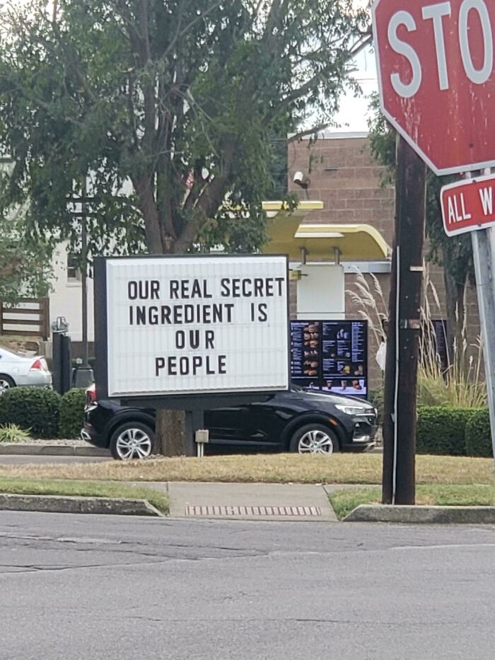 Absurd and hilarious sign at a drive-thru reading our real secret ingredient is our people on a street corner.