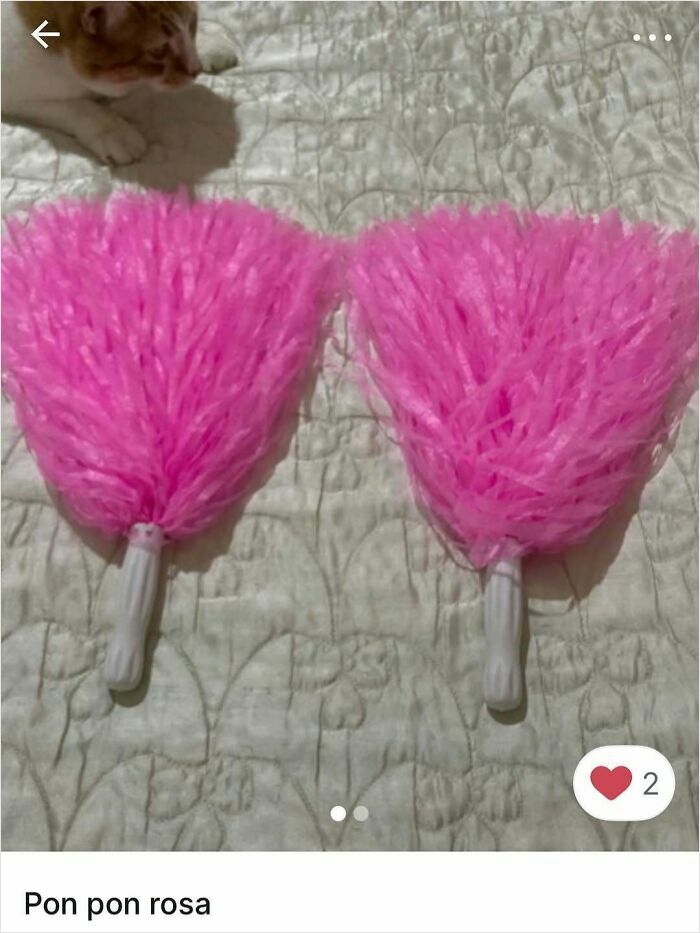 Cat near two bright pink pom poms on a quilted surface, showcasing playful moments in Vinted ads featuring cats.