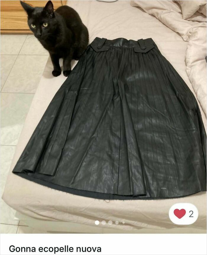 Black cat sitting on bed next to a pleated black skirt, showcasing cats stealing the spotlight in Vinted ads.