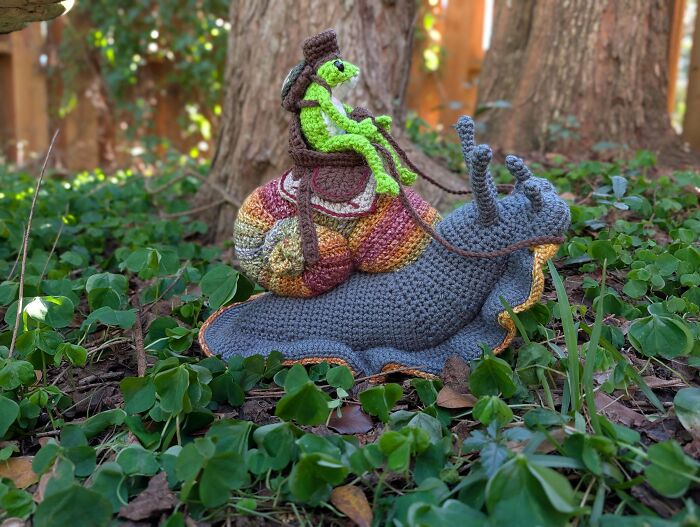 Awesome crocheted snail with a frog rider in a wooded setting. People crocheted something awesome.