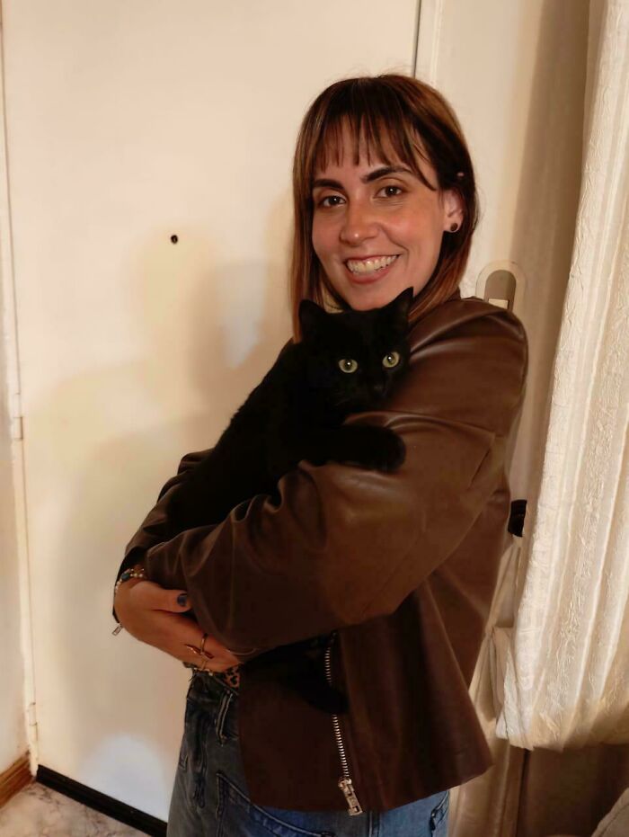 Woman smiling and holding a newly adopted black cat indoors during cozy winter beginnings for adopted pets.