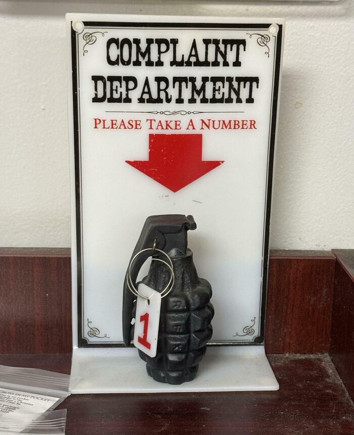 Humorous bizarre sign showing a complaint department with a hand g*****e keychain and number tag 1 for absurd complaints