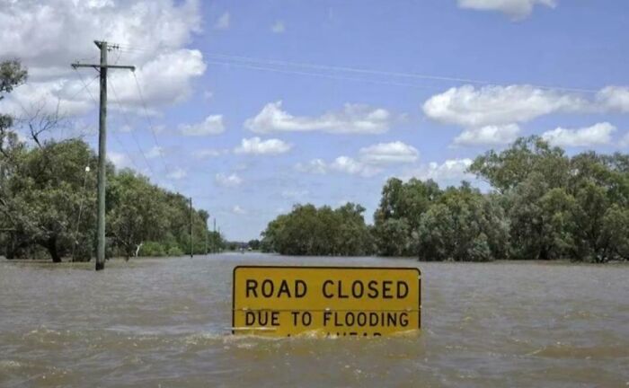 Flooded road with a yellow road closed sign partially submerged, illustrating bizarre and absurd signs not commonly seen.