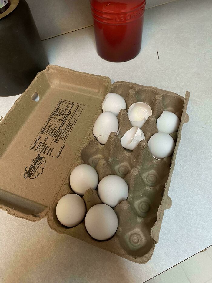 Carton of eggs with some c*****d and partially broken, showcasing an example of men being men in daily life.