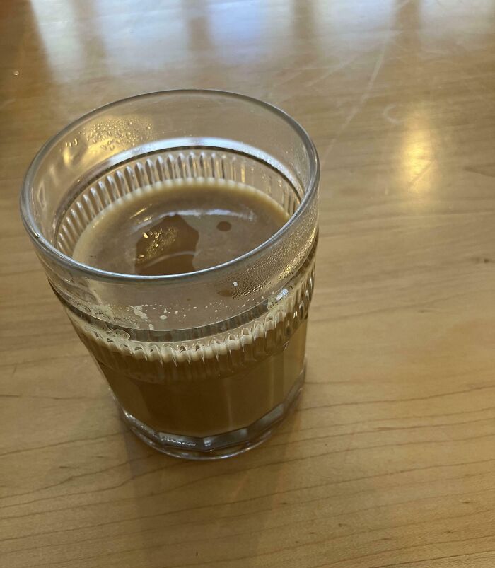 Glass of coffee with visible ice cubes on a wooden table illustrating infuriating examples of men being men.