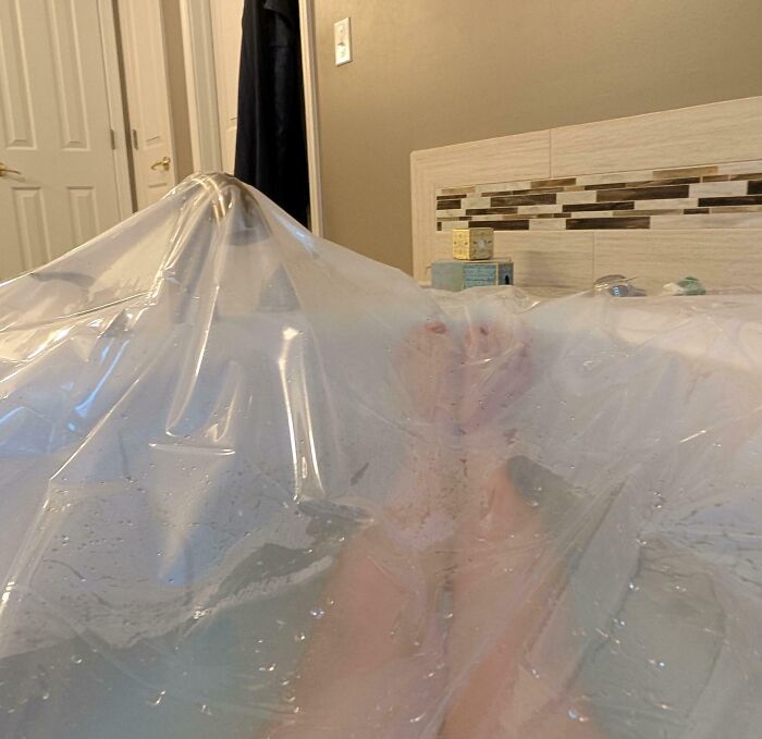 Feet covered by a clear plastic sheet in a bathtub, illustrating creative and unusual examples of if it works then it's not stupid.