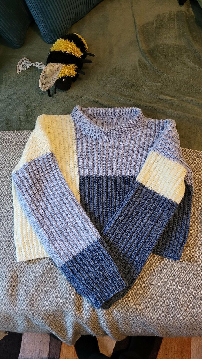 Awesome crocheted sweater in shades of blue and cream, with a bumblebee toy nearby. A handmade crochet project.