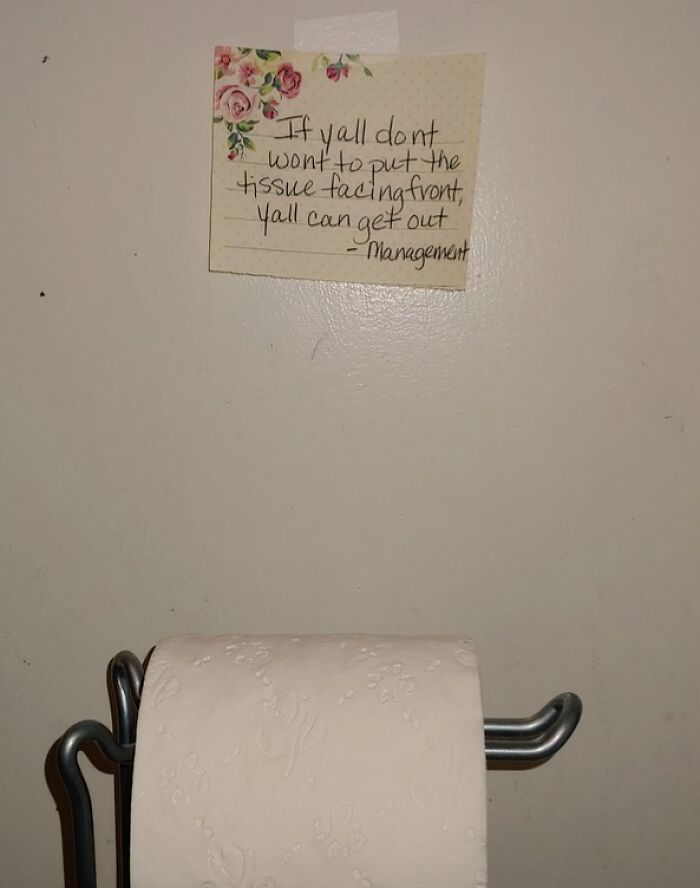 Handwritten creative note by parents above a toilet paper roll about putting the tissue facing front on the holder.
