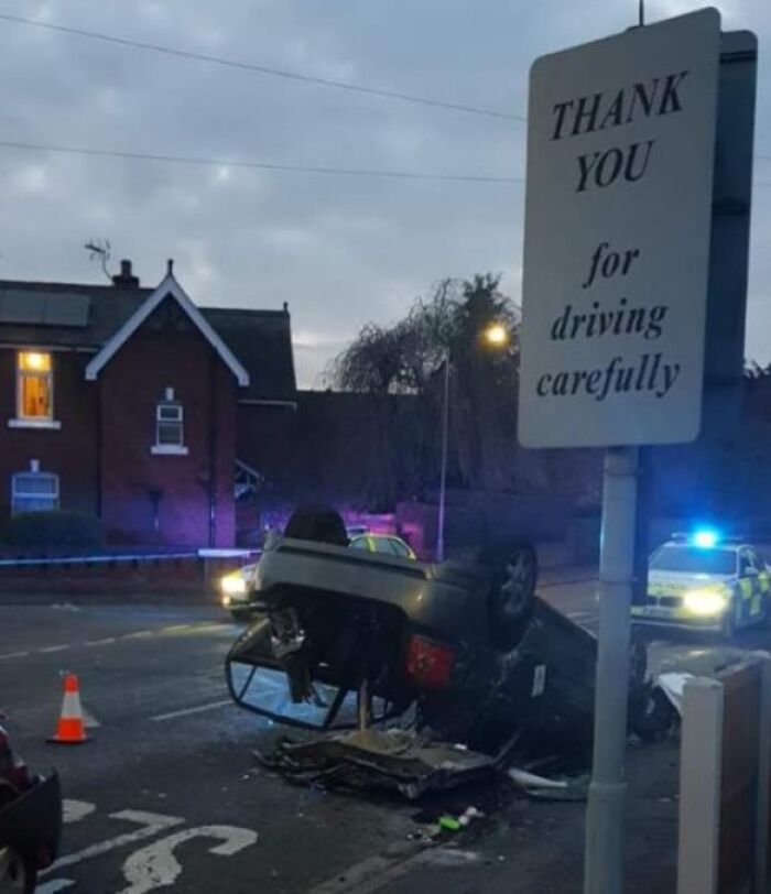 Overturned car accident under a sign reading thank you for driving carefully, highlighting dumb drivers shamed by people.