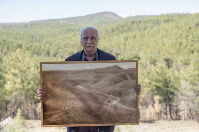 Elderly man holding a framed amazing photo of a barren landscape amidst a lush green forest, showing environmental change.