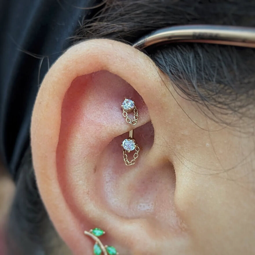 Close-up of an ear with a double industrial piercing featuring delicate chain jewelry, showcasing popular ear piercing types.