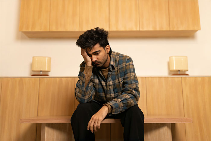 Man in a plaid shirt sitting on a bench looking frustrated, illustrating workplace bully revenge theatrics concept.