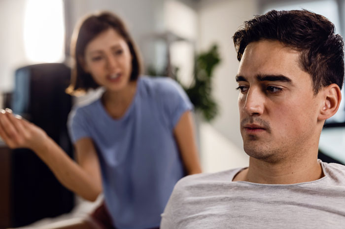 Woman forces boyfriend to sign contract demanding share of income, showing tension and serious expressions in a home setting.