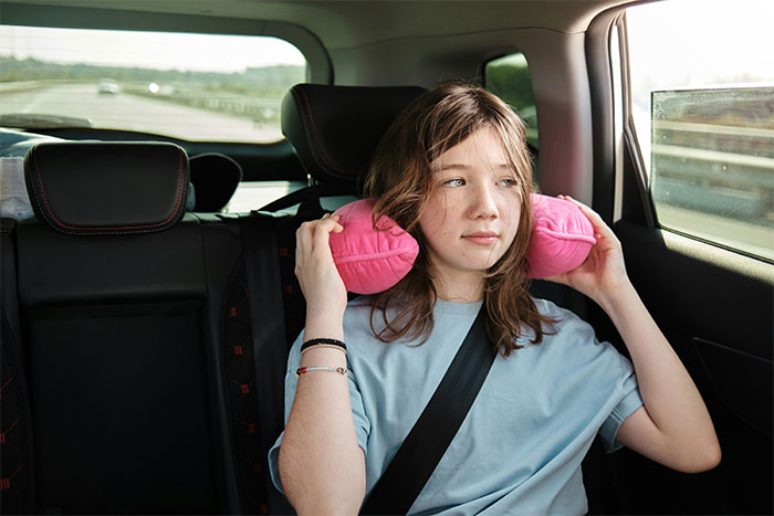 Teen girl with a pink neck pillow sitting in the backseat of a car, looking out the window, wearing a seatbelt. Teen girl with a pink neck pillow sitting in the backseat of a car, looking out the window, wearing a seatbelt.