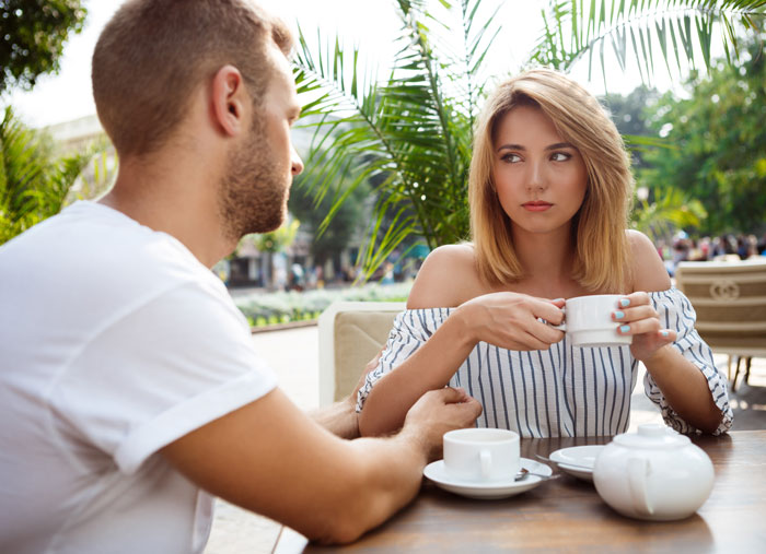 Woman unimpressed as man talks over coffee at outdoor cafe, dating deal breakers