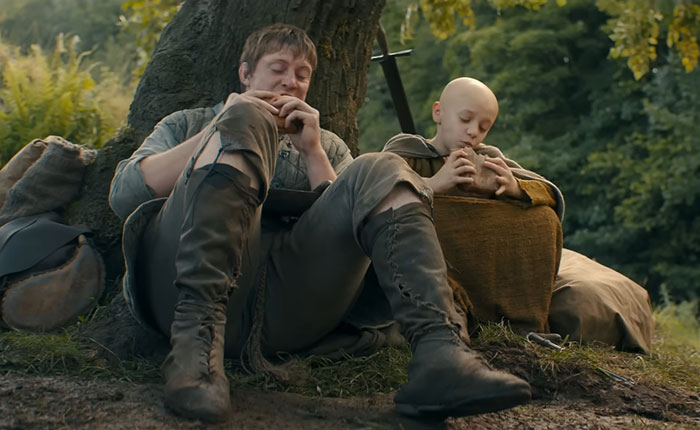Two characters from A Knight Of The Seven Kingdoms sitting by a tree, highlighting fan opinions on Rotten Tomatoes ratings.