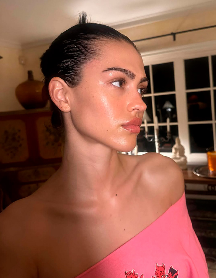 Woman with glowing skin and sleek hair in a softly lit room showcasing celeb facialist secrets for Golden Globes glow.