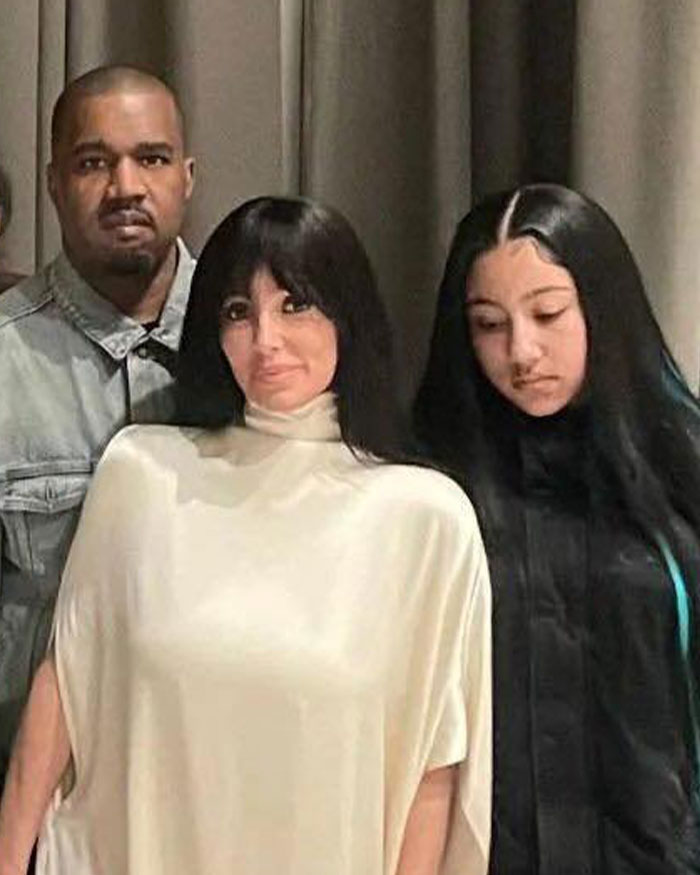 Kanye West standing behind Bianca Censori and North West who has a sad expression in a family photo indoors