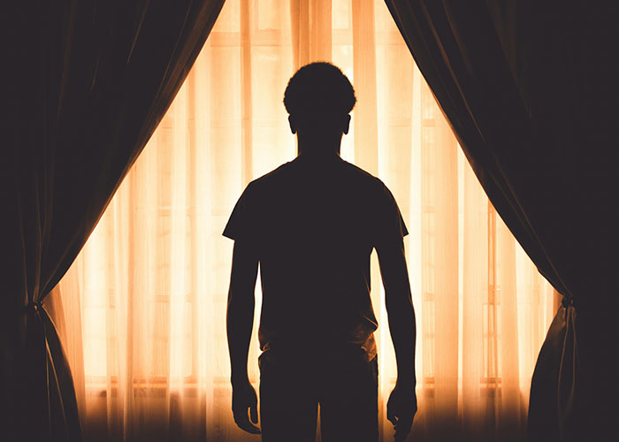 Silhouette of a person standing by a window with curtains, symbolizing reflection on being neurodivergent.