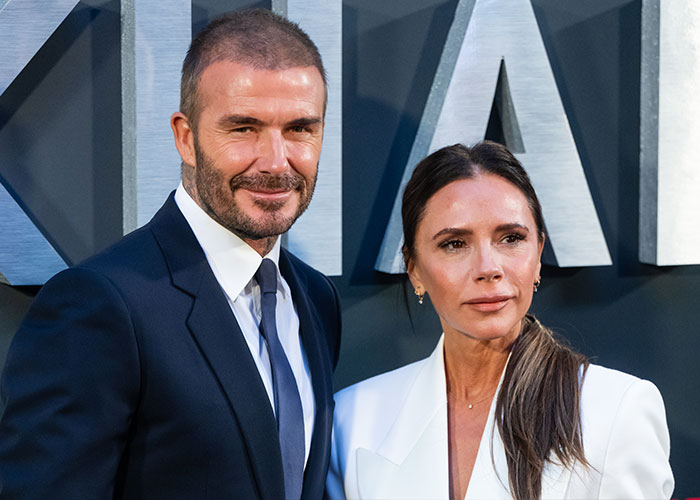 David Beckham and Victoria Beckham posing together at a formal event with a large sign in the background.