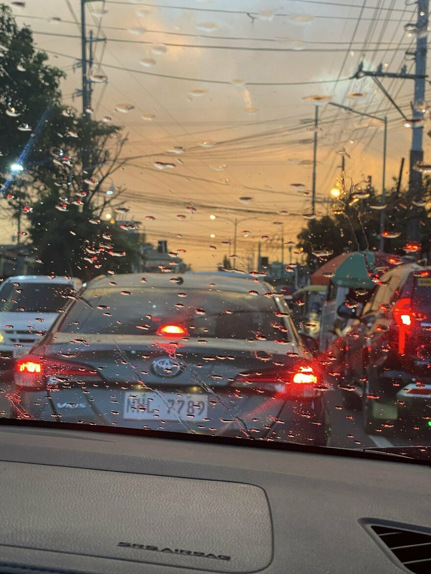 View through rain-covered car windshield showing heavy traffic and brake lights during evening rush hour in cities with worst traffic.