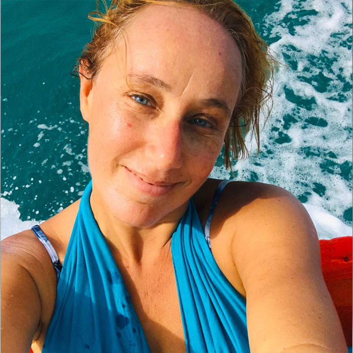 A woman in a blue top smiling with ocean waves in the background, representing intimacy surrogate challenges.