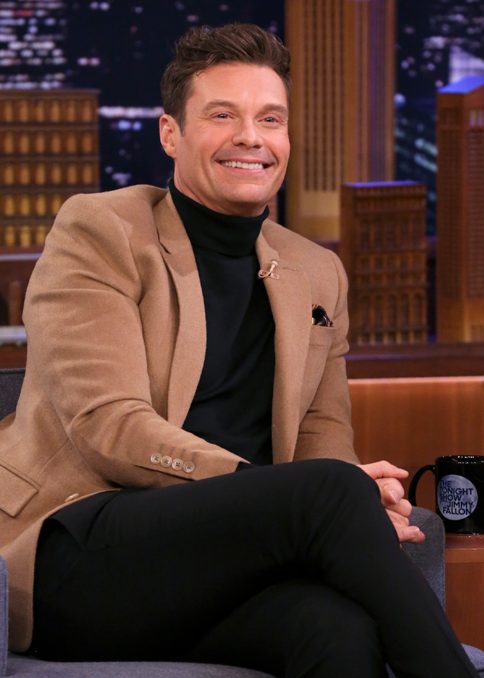 Ryan Seacrest smiling on a talk show set, wearing a tan blazer and black turtleneck, highlighting extremely skinny look.