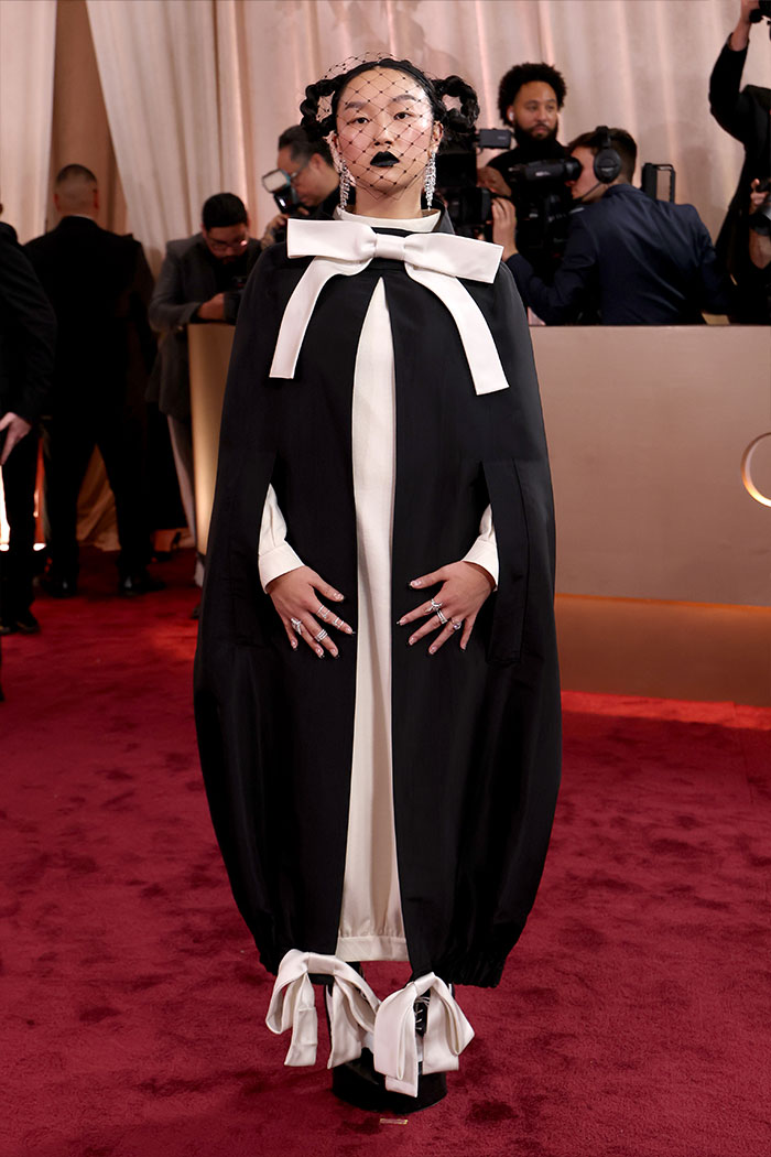Woman in bold black and white outfit with veil and large bows poses at red carpet fashion disasters event.