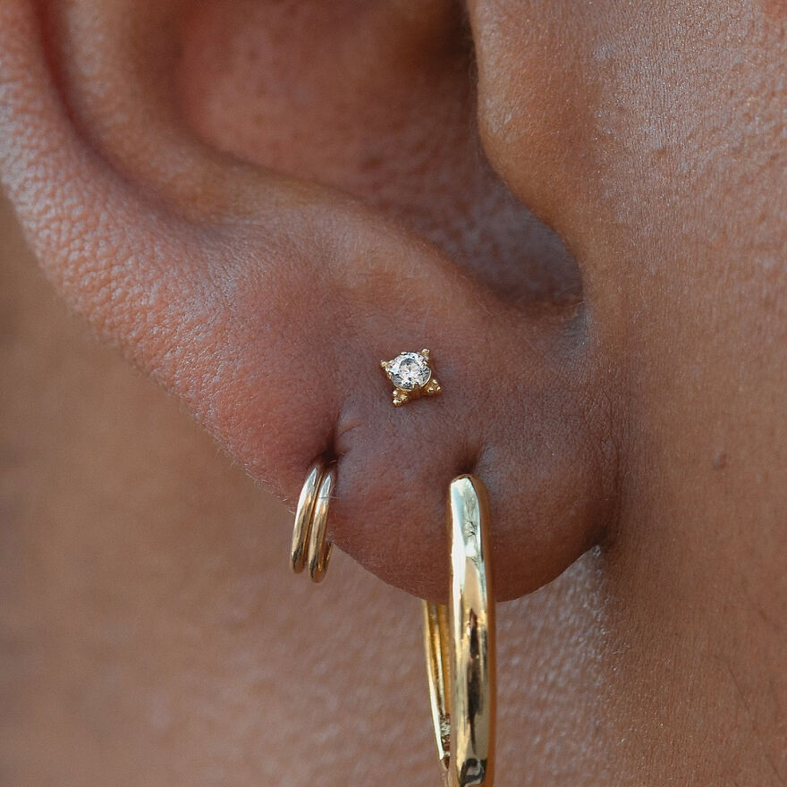 Close-up of an ear showing multiple types of ear piercing with gold hoops and a diamond stud earring.