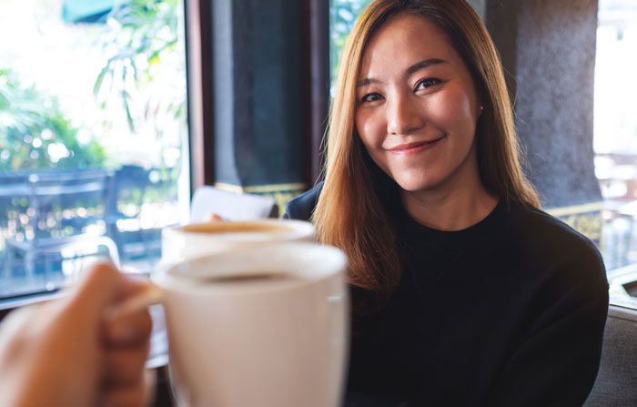 Woman smiling in a cafe holding a coffee cup, representing a contract for a share of her boyfriend's income.