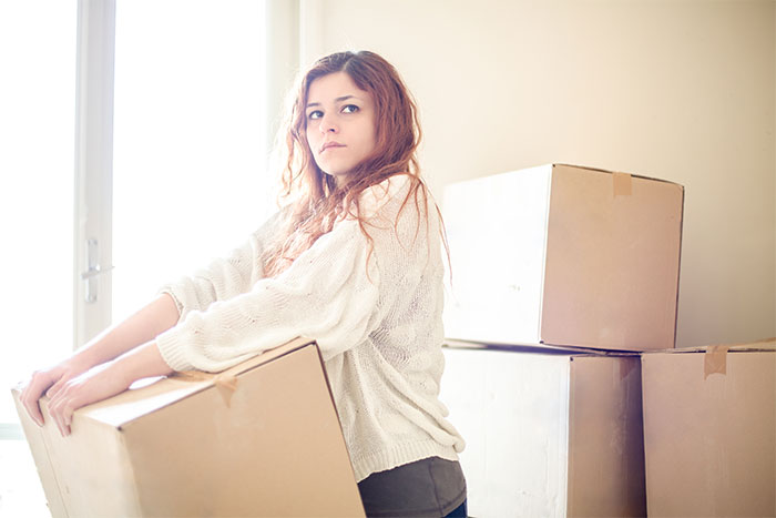 Young woman moving cardboard boxes indoors, symbolizing entitled sister and family tenant harassment conflict scenario.