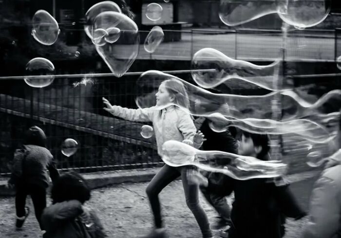 Children playing with large soap bubbles in a street scene capturing unexpected and beautiful moments of life.