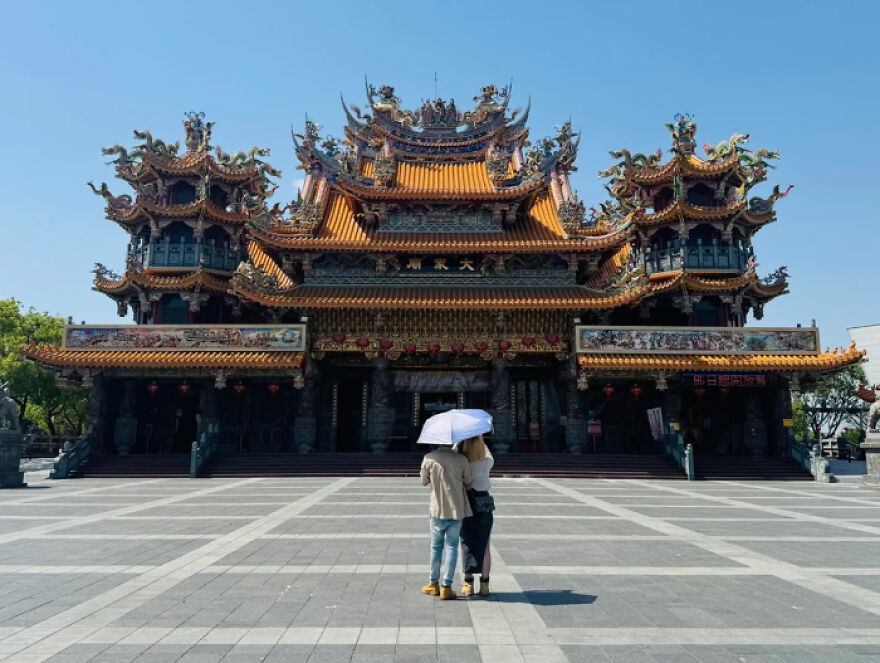 Traditional Asian temple with intricate roof details and two people standing under an umbrella, representing cities with worst traffic.