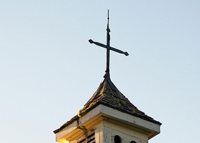 Old church steeple with a weathered cross against a clear sky, symbolizing silent revenge acts and hidden stories.