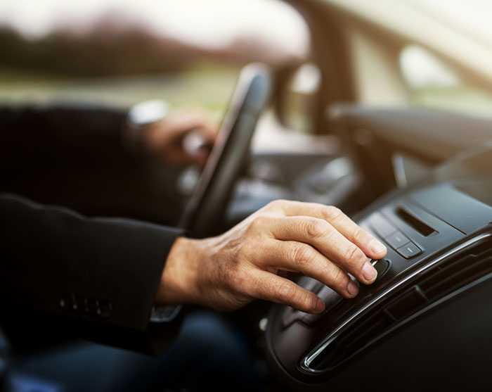 Man in a car adjusting controls on the dashboard with focus on the hand and phone hidden nearby.
