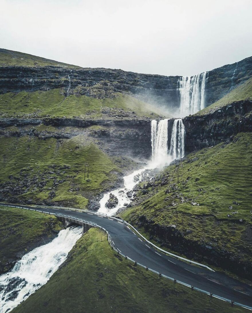 Scenic waterfall and winding road in lush green landscape, showcasing one of the best places you should visit at least once.