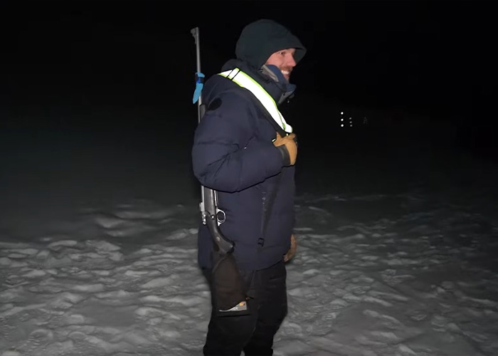 Content creator exploring the world&rsquo;s darkest island at night, dressed warmly with a rifle on snowy terrain.