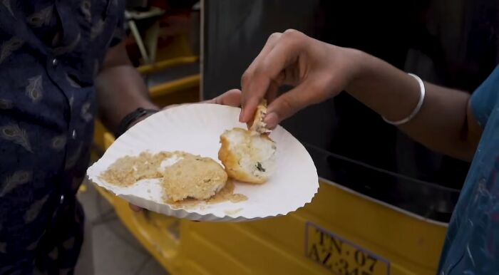 A person eating street food from a paper plate, showing cultural habits that may be normal or offensive in different countries.