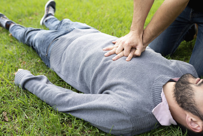 Person performing CPR on a man lying on grass, illustrating the impact of SOS code on rescue missions.