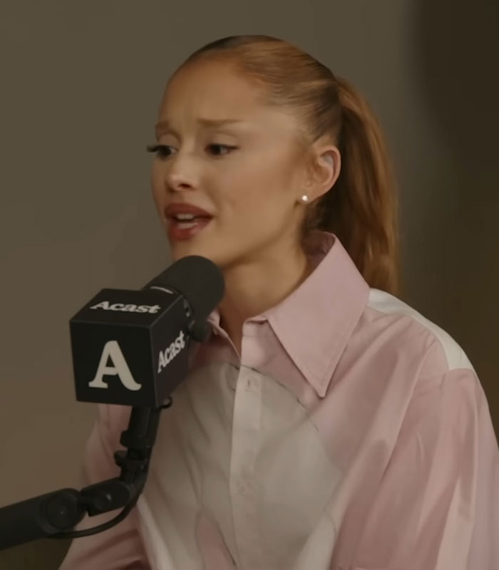 Ariana Grande speaking into Acast microphone during a podcast discussing resurfaced performance fan backlash moments.