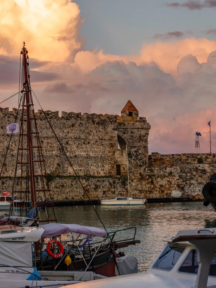 Ancient stone fortress by a harbor with boats at sunset, related to countries that sleep the most OECD data.