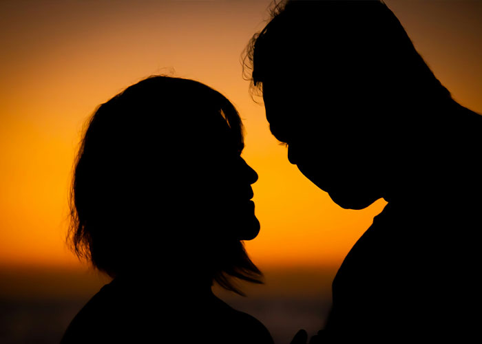 Silhouettes of a couple facing each other at sunset, illustrating intimacy surrogate challenges on the job.