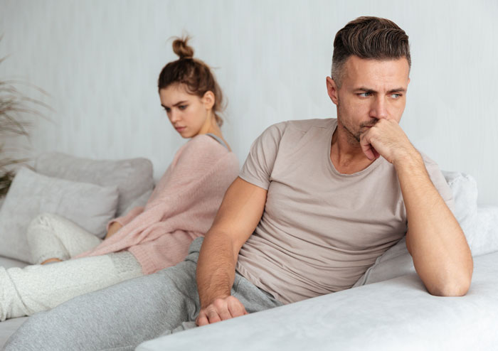 Couple sitting apart on couch looking upset, illustrating relationship tension after cheating was discovered involving the phone.