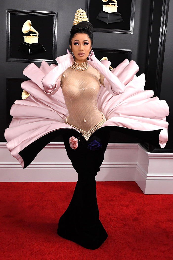 Artist wearing a dramatic pink and black dress with pearl details at the wild Grammys looks on the red carpet.